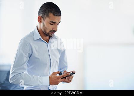 Sempre raggiungibile. un giovane uomo d'affari che invia un messaggio di testo mentre è in ufficio Foto Stock