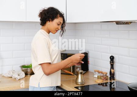 Sonnolenta donna afroamericana che fa caffè macinato a casa in cezve turco Foto Stock