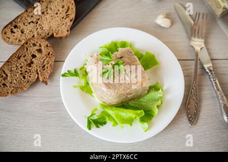 Carne di pollo lessata aspica in brodo di gelatina di carne in un piatto su un tavolo di legno Foto Stock