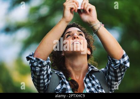 La donna scatta foto overhead con il suo telefono cellulare, forse è birdwatching o ha visto un piccolo animale carino nei boschi e vuole prendere souvenir di h Foto Stock