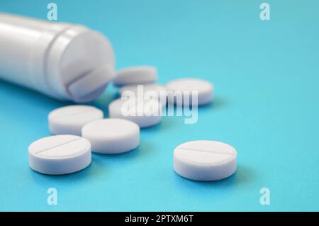 Diverse compresse bianche ricade al di fuori del vaso in plastica sulla superficie blu. Immagine di sfondo sul farmaceutico e medico, argomenti Foto Stock