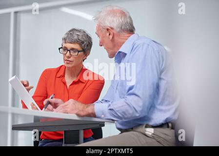 Affrontare insieme le sfide aziendali. due colleghi aziendali maturi seduti con un tablet digitale per discutere del lavoro Foto Stock