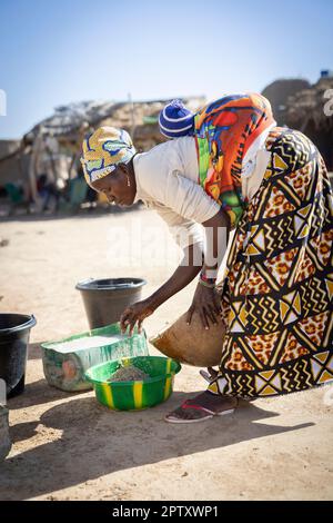 Una donna africana lava il suo raccolto di miglio mentre porta il suo bambino sulla schiena nella regione di Segou, Mali, Africa occidentale. 2022 siccità del Mali e crisi della fame. Foto Stock