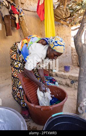 Una madre lava i vestiti a casa sua mentre porta il suo bambino neonato sulla schiena nella regione di Segou, in Mali, in Africa occidentale. 2022 siccità del Mali e crisi della fame. Foto Stock