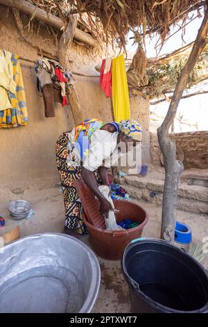 Una madre lava i vestiti a casa sua mentre porta il suo bambino neonato sulla schiena nella regione di Segou, in Mali, in Africa occidentale. 2022 siccità del Mali e crisi della fame. Foto Stock