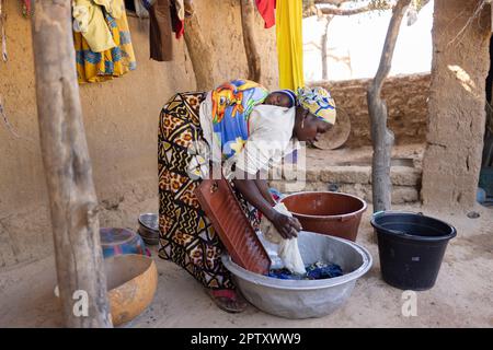 Una madre lava i vestiti a casa sua mentre porta il suo bambino neonato sulla schiena nella regione di Segou, in Mali, in Africa occidentale. 2022 siccità del Mali e crisi della fame. Foto Stock