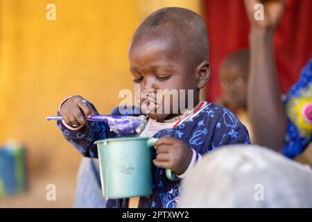 Un bambino affamato mangia un pasto di porridge di miglio da una tazza nella regione di Segou, Mali, Africa occidentale. 2022 siccità del Mali e crisi della fame. Foto Stock