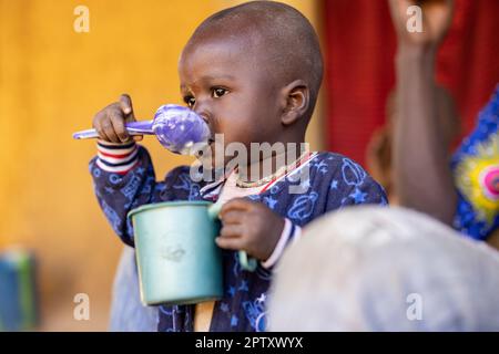 Un bambino affamato mangia un pasto di porridge di miglio da una tazza nella regione di Segou, Mali, Africa occidentale. 2022 siccità del Mali e crisi della fame. Foto Stock