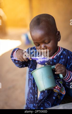 Un bambino affamato mangia un pasto di porridge di miglio da una tazza nella regione di Segou, Mali, Africa occidentale. 2022 siccità del Mali e crisi della fame. Foto Stock