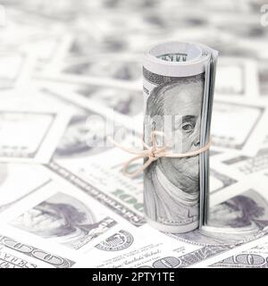 US dollari arrotolata e serrato con band giace su un sacco di banconote americane con sfondo sfocato. Grandi quantità di denaro Foto Stock