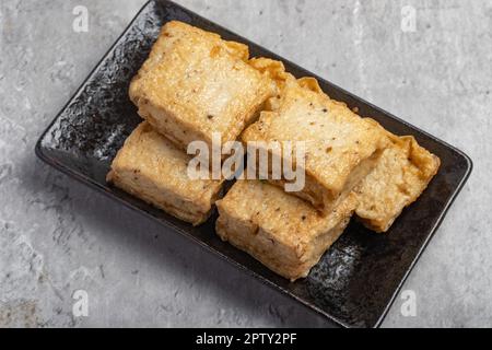 Il tofu di sesamo nero fritto in un piatto nero Foto Stock