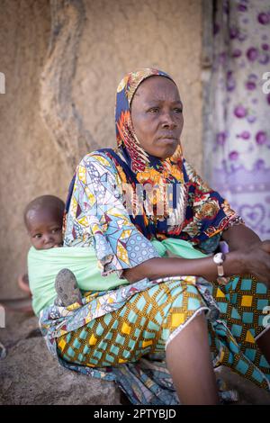 Una donna anziana in abito tradizionale africano porta suo nipote sulla schiena in una fionda nella regione di Segou, Mali, Africa occidentale. 2022 siccità del Mali e crisi della fame. Foto Stock