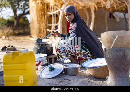 Una giovane rifugiata Fulani, sfollata dal conflitto nel Nord, bolle cibo su un fuoco aperto nella regione di Segou, Mali, Africa occidentale. 2022 siccità del Mali e crisi della fame. Foto Stock