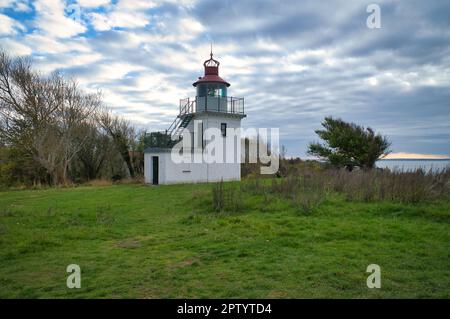 Faro, Spodsbjerg Fyr a Huntsted sulla costa della Danimarca. I raggi del sole brillano attraverso le nuvole. Prato con alberi. Foto di paesaggio dal mare Foto Stock