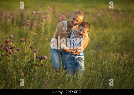 Due fratelli ragazzi felici sulla strada steppa sullo sfondo di erba alta gialla e verde. Vacanze estive. Buon concetto di estate Foto Stock