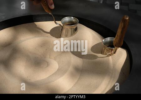 Caffè preparato su sabbia calda - caffè turco preparato in un Turk, primo piano. Processo di preparazione del caffè fragrante, focalizzazione selettiva Foto Stock