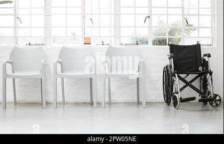 Diversity, inclusive e una fila di sedie bianche con una sedia a rotelle nera in una sala d'attesa in ospedale. Diversi posti a sedere vuoti all'interno di una lobby di A. Foto Stock