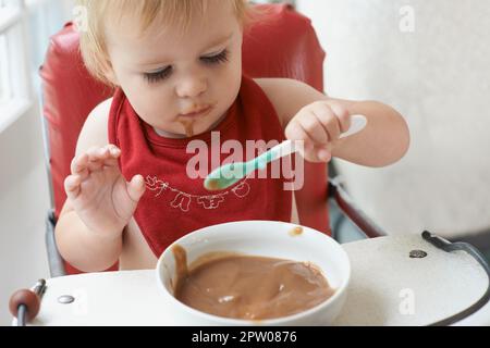 Il ragazzo in crescita ha bisogno del suo cibo. Un bambino giovane che mangia al suo cuore contenuto nella sua seggiolone Foto Stock