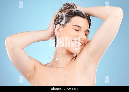 Bellezza, doccia e donna lavare i capelli con gocce d'acqua su uno sfondo blu studio con cosmetici, shampoo e sapone per il corpo fresco e pulito. Igiene, Foto Stock