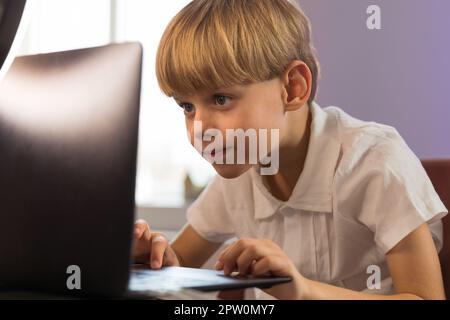Felice ragazzo seduto alla sua scrivania con un computer portatile. Foto di alta qualità Foto Stock