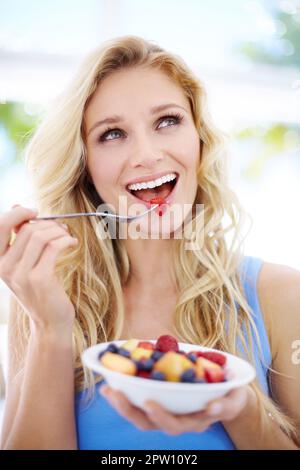 Anticipando un gusto delizioso. Bella giovane donna che guarda in su mentre mangia la sua insalata di frutta Foto Stock