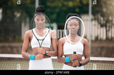 Giocatori seri di tennis che tengono le loro racchette. Ritratto dei giovani tennisti che ricoprono il volto con racchette sul campo. Ragazze afroamericane Foto Stock