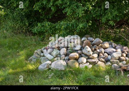 Pietre grandi impilate o rocce su un campo di erba verde. Rocce lungo un remoto sentiero escursionistico in natura. Cumulo raccolto di pietre che segnano il terreno forestale, Foto Stock