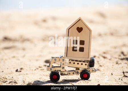 Un'automobile da un costruttore di metallo trasporta una piccola casa decorativa sulla sabbia, comprando il bene immobile, una casa sulla sabbia in Ucraina Foto Stock