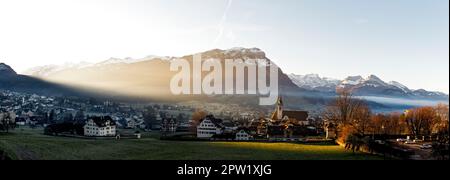 Mattina foschia o sera foschia con i raggi luminosi del sole che la penetrano nella città di Schwyz in Svizzera Foto Stock