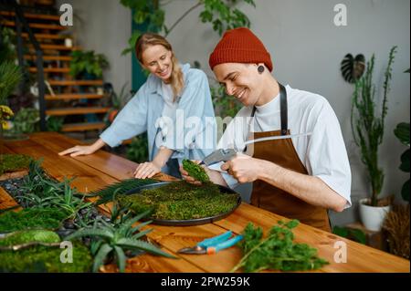 Fiorista donna che insegna giovane uomo hipster decoratore come comporre pezzo muschio su piatto al laboratorio artigianale studio d'arte Foto Stock