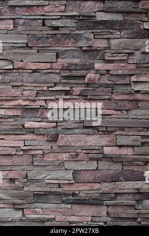 La texture di un muro di pietra dal lungo e le pietre grezze di diverse dimensioni e di toni Foto Stock