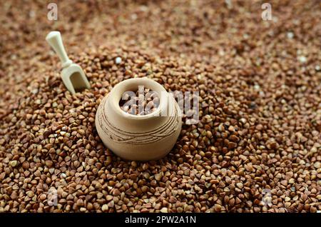 Immagine di sfondo di un gran mucchio di grano saraceno, al centro del quale si trova una piccola brocca e una spatola in legno per i cereali Foto Stock