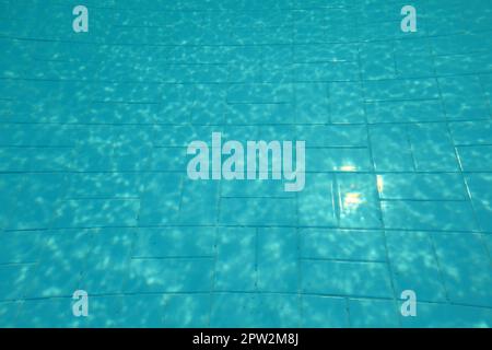 Piscina fondo, il sole che splende su piastrelle blu, linee distorta dalla rifrazione in acqua. Foto Stock