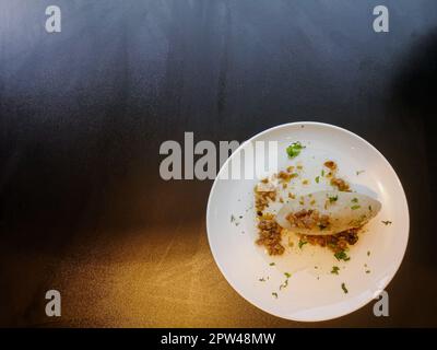 Zeppeline o Cepelinai o cepeline o didzkukuliai con pancetta fritta ed erbe su piatto bianco su tavolo nero Foto Stock