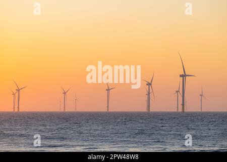 Grandi turbine eoliche che producono impianti in mare al tramonto Foto Stock