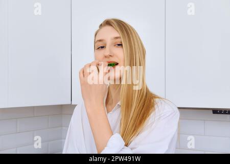 Donna difficile mordere pezzo di cetriolo mentre si fa insalata di verdure Foto Stock