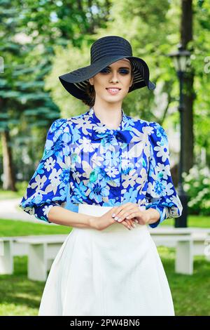 Ritratto all'aperto di una ragazza sorridente in berretto nero, blusa blu e gonna bianca. Foto Stock