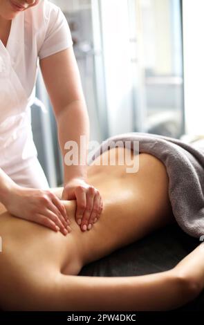 Master senza volto che dà massaggio di muscoli della schiena e delle spalle a. donna anonima sdraiata sul tavolo nel salone termale Foto Stock