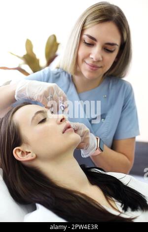 Estetista professionista che inietta acido ialuronico vicino agli occhi della donna durante procedura anti invecchiamento in clinica di bellezza Foto Stock