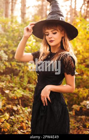 Giovane donna in nero guardando via il giorno di Halloween nella foresta autunnale Foto Stock