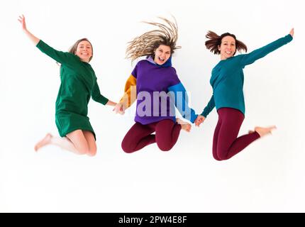 Immagine di tre donne allegre a piedi nudi di diversa età che tengono le mani insieme, saltando e divertendosi, godendo la vacanza, festeggiando Foto Stock