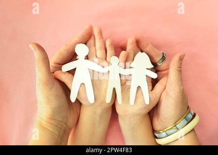 Colpo corto di madre, padre e bambino che tiene carta di famiglia ritagliata nelle mani, isolato su sfondo rosa. figure di cartone di genitori e capretto Foto Stock