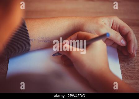 Scatto ritagliato dello studente utilizzando il foglio di trucco per l'esame di matematica, leggendo la formula scritta a portata di mano mentre truffa durante il test in università o scuola, selettivo Foto Stock