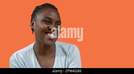 Primo piano ritratto di felice giovane donna africana che guarda a destra con grande sorriso, indossando t-shirt bianca e capelli mordente, su sfondo arancione con Foto Stock