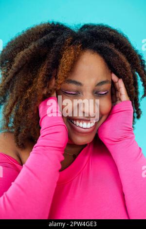 Sognante giovane bella ragazza afroamericana con gli occhi luminosi che indossano il bodysuit rosa sopra la parete blu tiene le mani pressate insieme sotto il mento Foto Stock