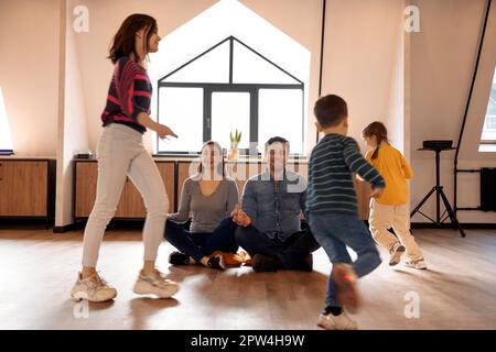 I genitori che si rilassano sono seduti sul pavimento e meditano mentre ci sono tre bambini che corrono in tutto l'appartamento. Mentre le figlie e il figlio rumoroso Foto Stock