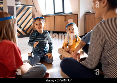 Famiglia giovane felice con i bambini che giocano un gioco di carte a casa seduti sul pavimento. Madre, padre, figlio e figlie che giocano a carte in soggiorno Foto Stock
