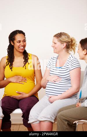 Lei ha il nostro sostegno. Un gruppo multietnico di donne incinte sorridenti l'una contro l'altra mentre si siedono e toccano le loro pance Foto Stock