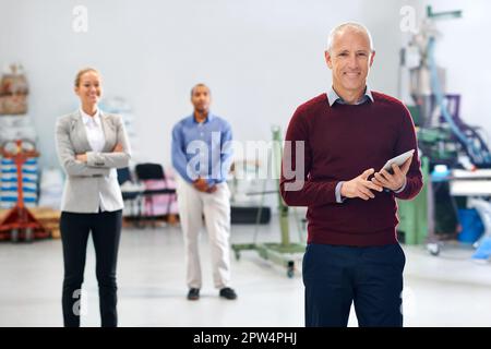 Gestire la fabbrica con sicurezza e poise. Un manager che utilizza un tablet durante un'ispezione in fabbrica con i suoi colleghi in background Foto Stock