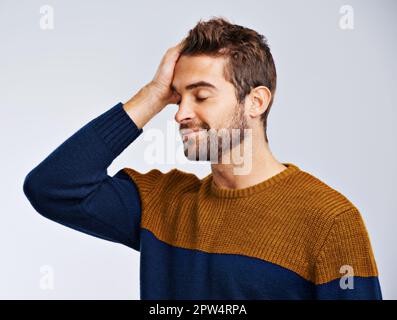 Non ho pensato tutto questo. Studio shot di un giovane che guarda con rammarico su uno sfondo grigio Foto Stock